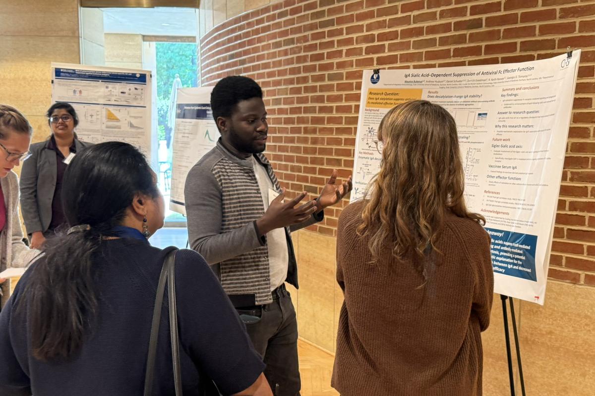   Poster session participant, Maurice Bukenya explains a poster to Kelly Seaton and another attendee. 